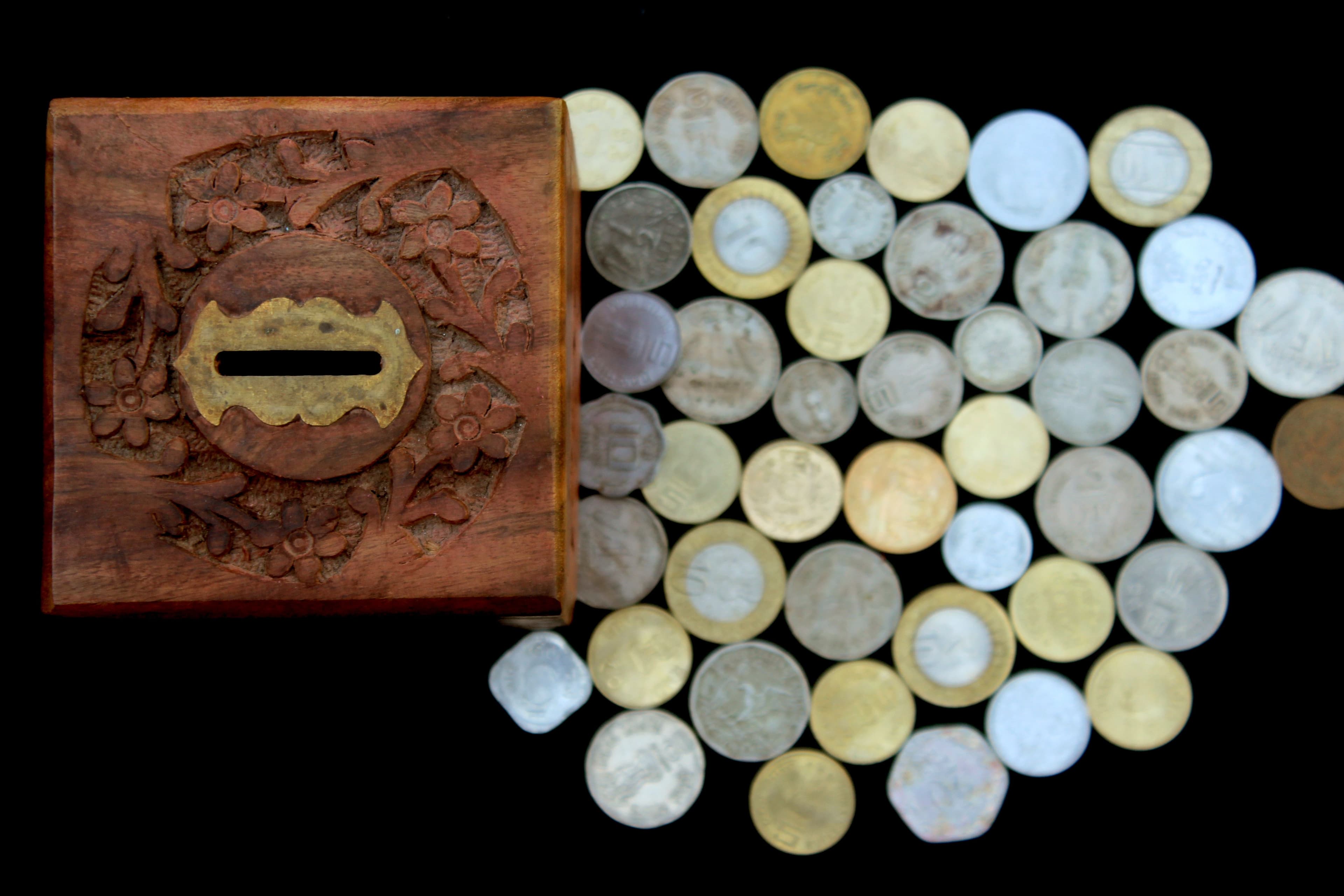 A wooden savings box surrounded by coins